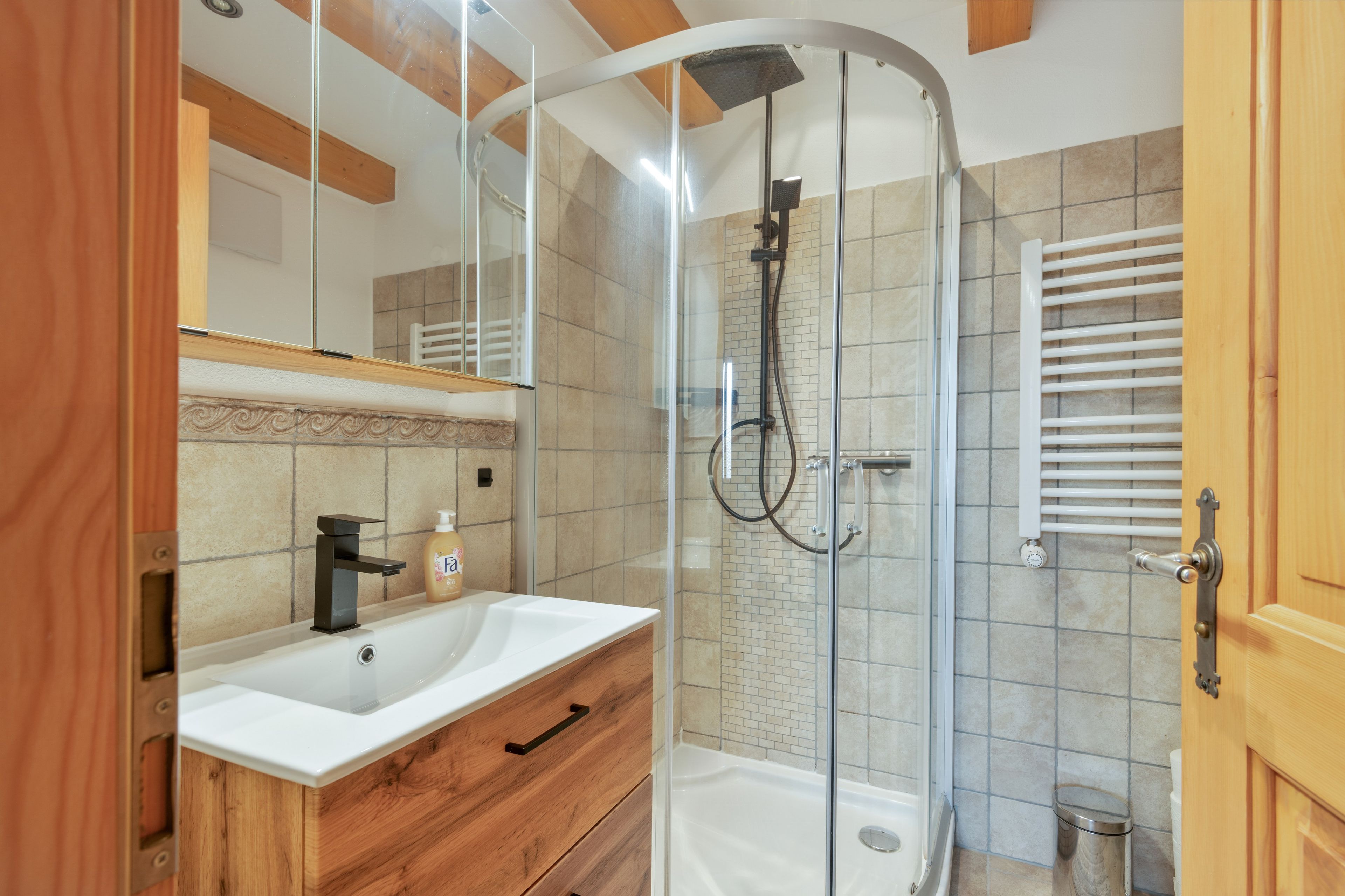 A modern bathroom with a glass-enclosed shower, a wooden vanity, and a white sink.