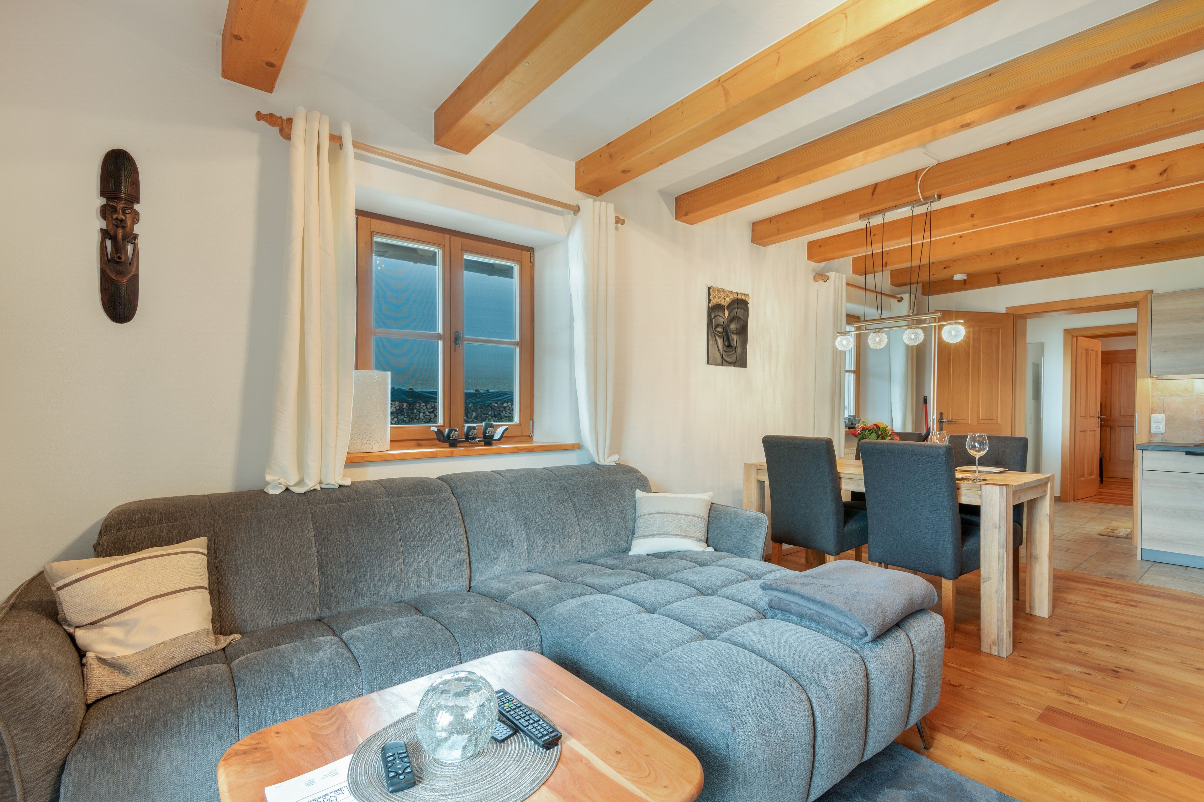 A modern living room with a grey sofa, a wooden coffee table, and a dining area with a wooden table and chairs.