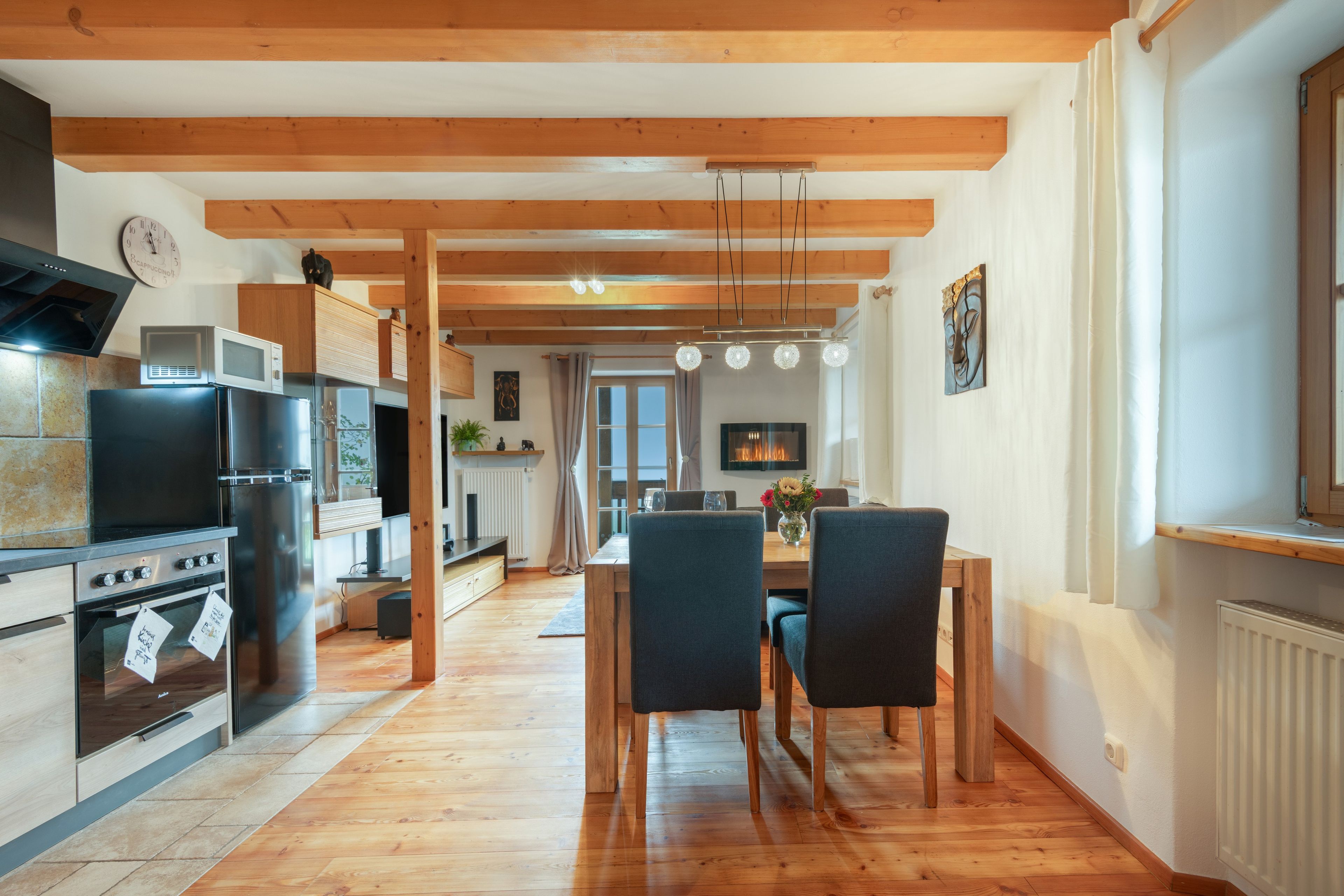 A modern kitchen with wooden beams, stainless steel appliances, and a dining area with a wooden table and chairs.