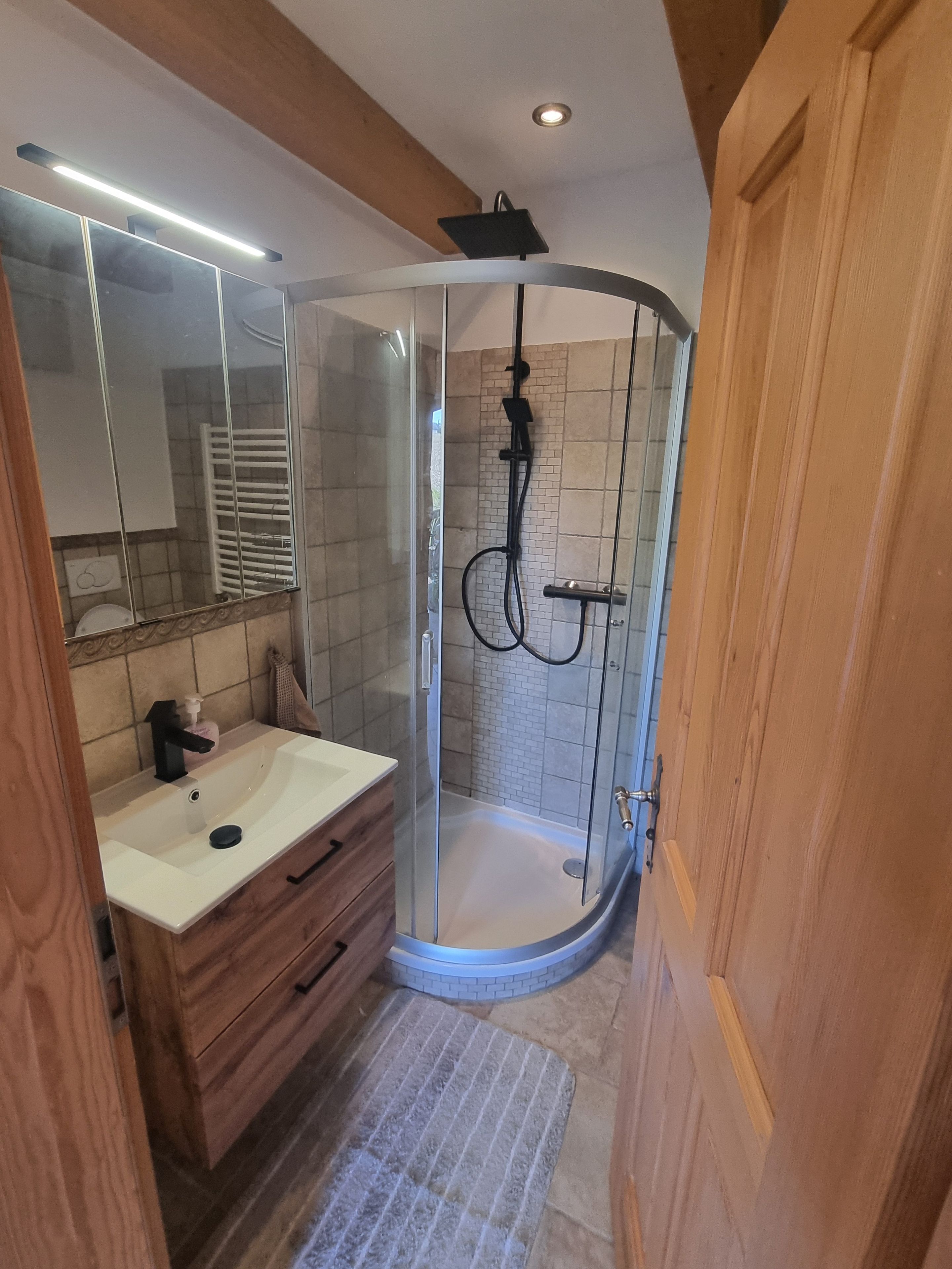 Un baño moderno con ducha de vidrio, lavamanos blanco, muebles de madera y un espejo.