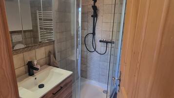 Un baño moderno con ducha de vidrio, lavamanos blanco, muebles de madera y un espejo.