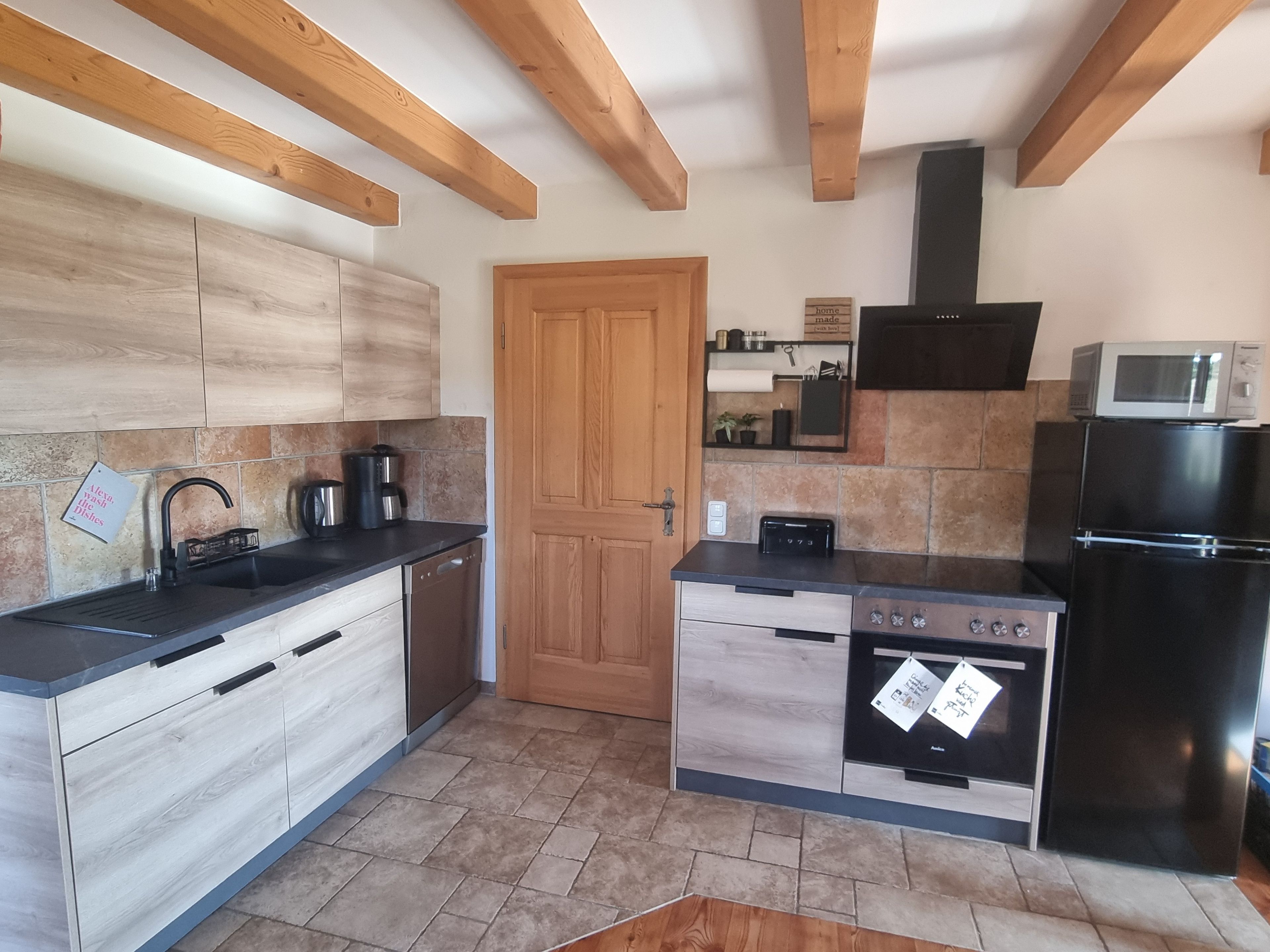 A modern kitchen with wooden beams, a black refrigerator, a microwave, a stove, and a sink.