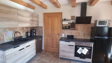 A modern kitchen with wooden beams, a black refrigerator, a microwave, a stove, and a sink.