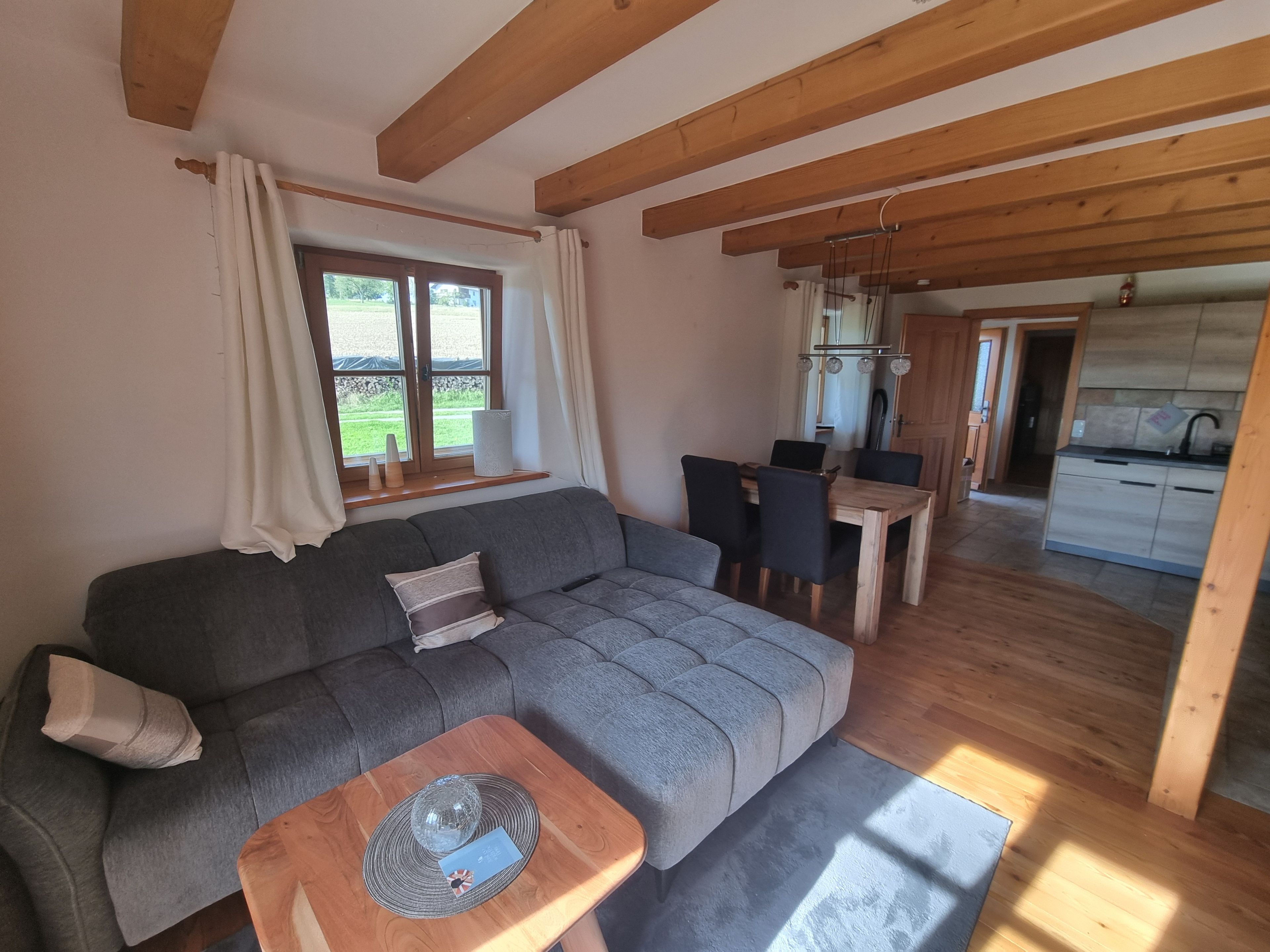 A cozy living room with a grey sofa, a wooden coffee table, and a dining area with a wooden table and chairs.