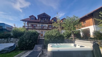 Una cabaña de dos pisos con terraza de madera, bañera de hidromasaje y un muro de piedra.