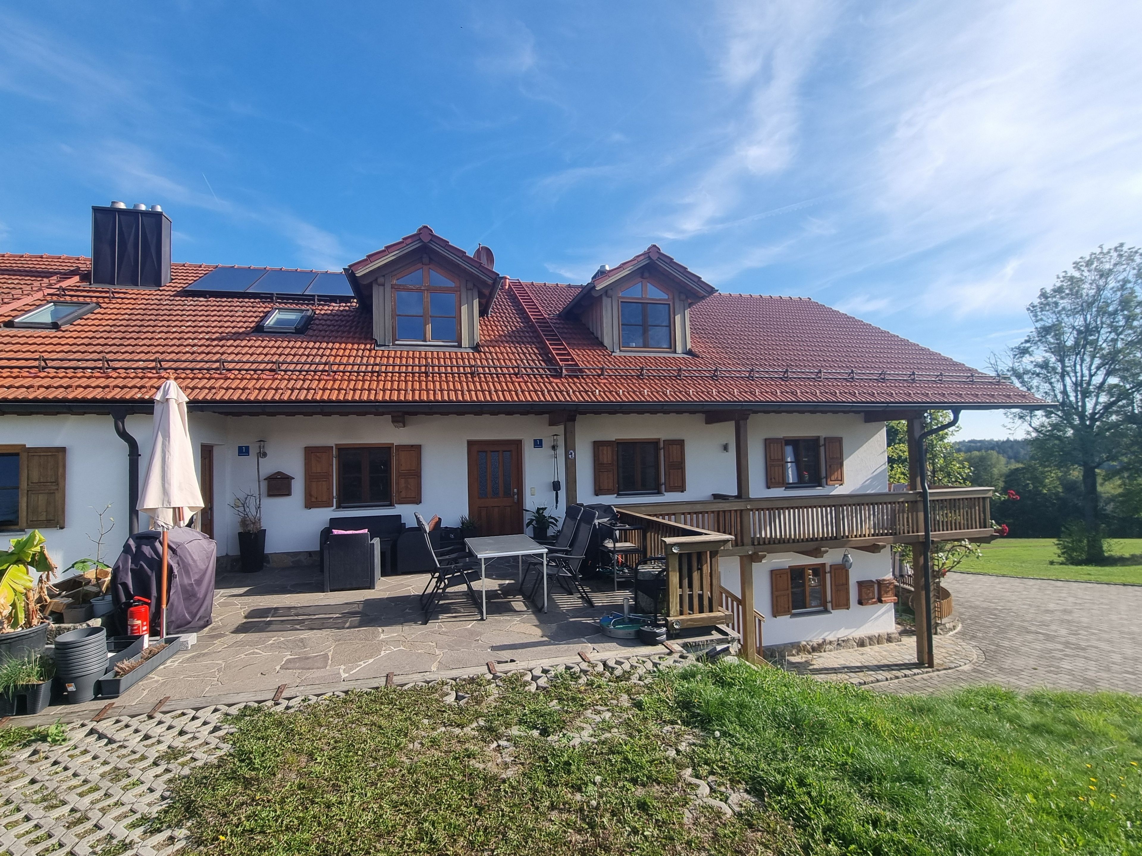 A two-story house with a red-tiled roof, a balcony, and a patio area with outdoor furniture.