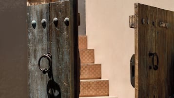 A wooden gate leading to a staircase with a beige wall and a potted plant in the background.