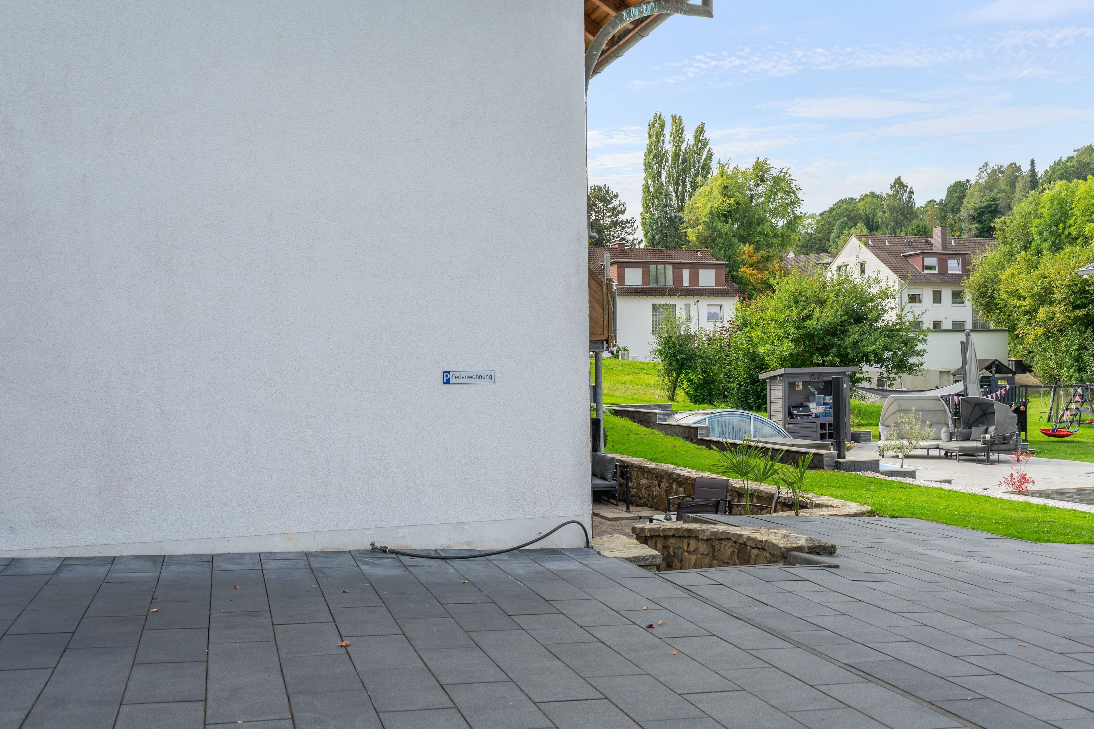 Ein gepflasterter Außenbereich mit einer Steinmauer, einer kleinen Sitzecke mit Tisch und Stühlen sowie einem Schild, das einen Parkplatz kennzeichnet.
