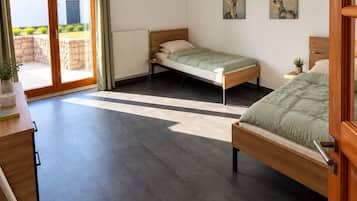 Ein modernes Schlafzimmer mit zwei Betten, einem Schreibtisch und einer Glasschiebetür, die zu einem Außenbereich führt.