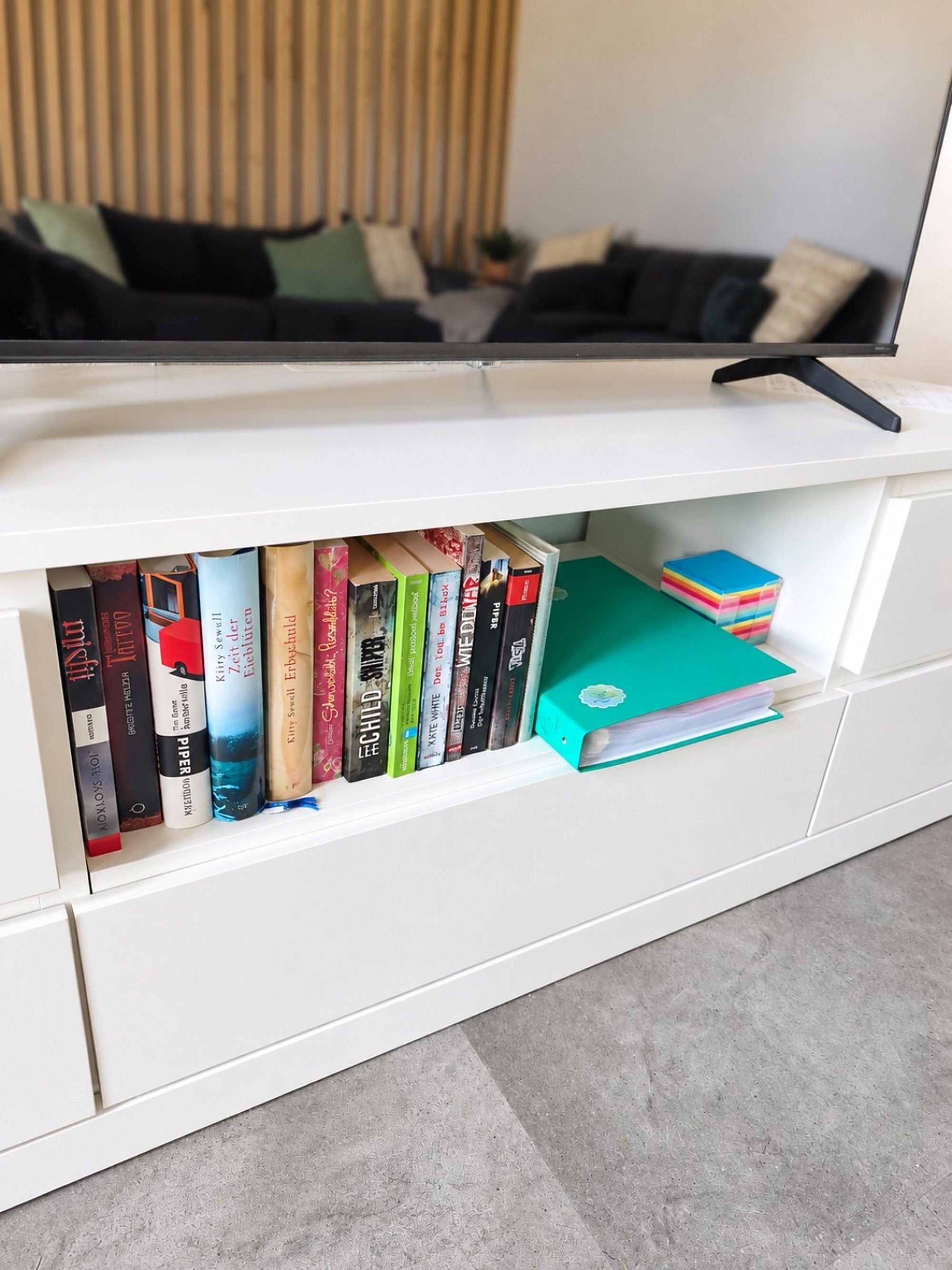 Eine weiße Unterhaltungsanlage mit Fernseher obenauf und einem Bücherregal darunter.