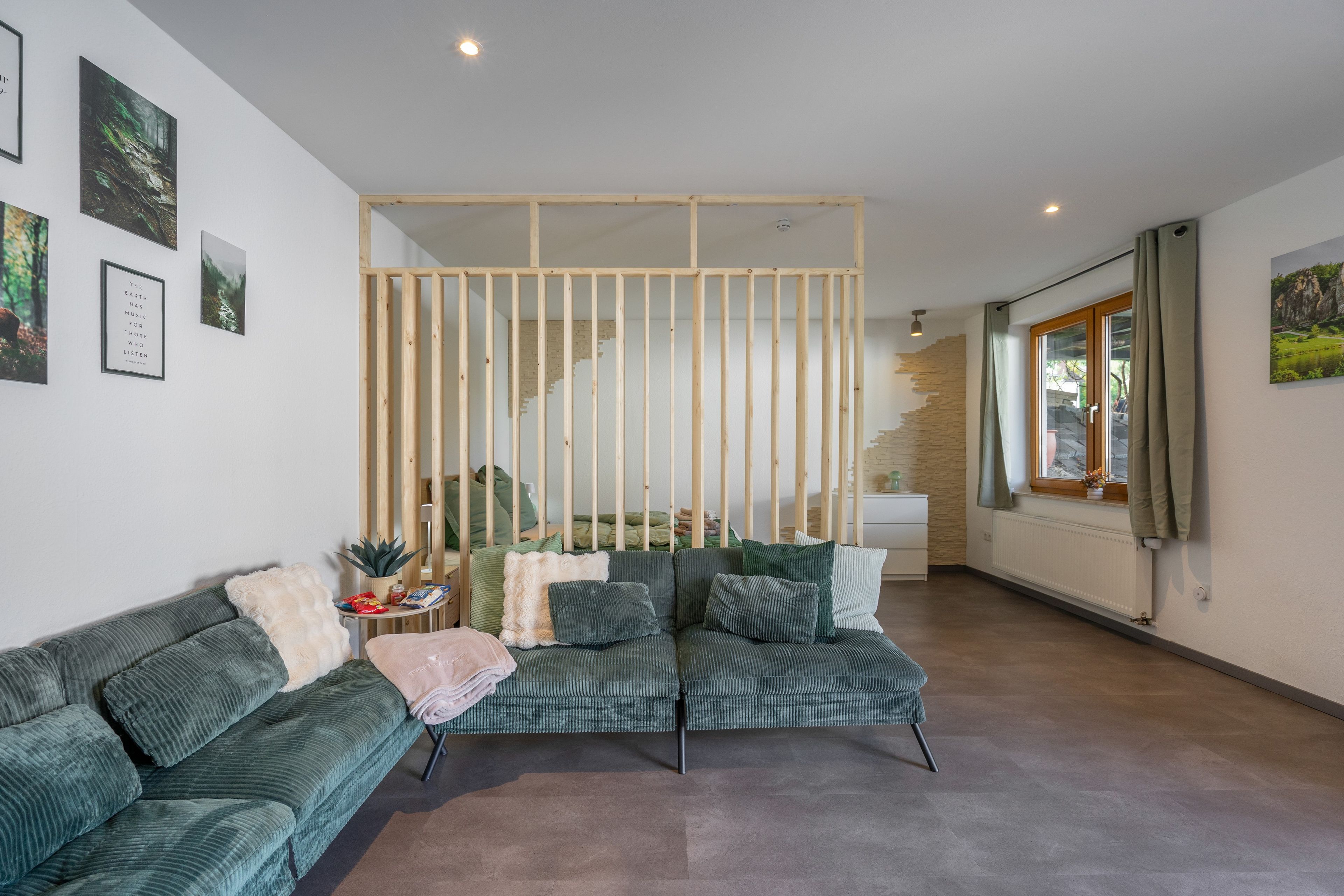 Een moderne woonkamer met een groene bank, een houten scheidingswand en een trap naar een hoger gelegen verdieping.