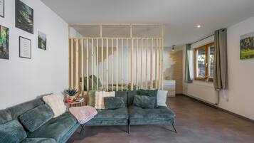 Een moderne woonkamer met een groene bank, een houten scheidingswand en een trap naar een hoger gelegen verdieping.