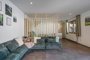 A modern living room with a green sofa, a wooden partition, and a staircase leading to an upper level.