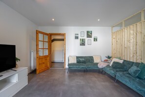 A modern living room with a green sofa, a television, and a wooden door leading to another room.