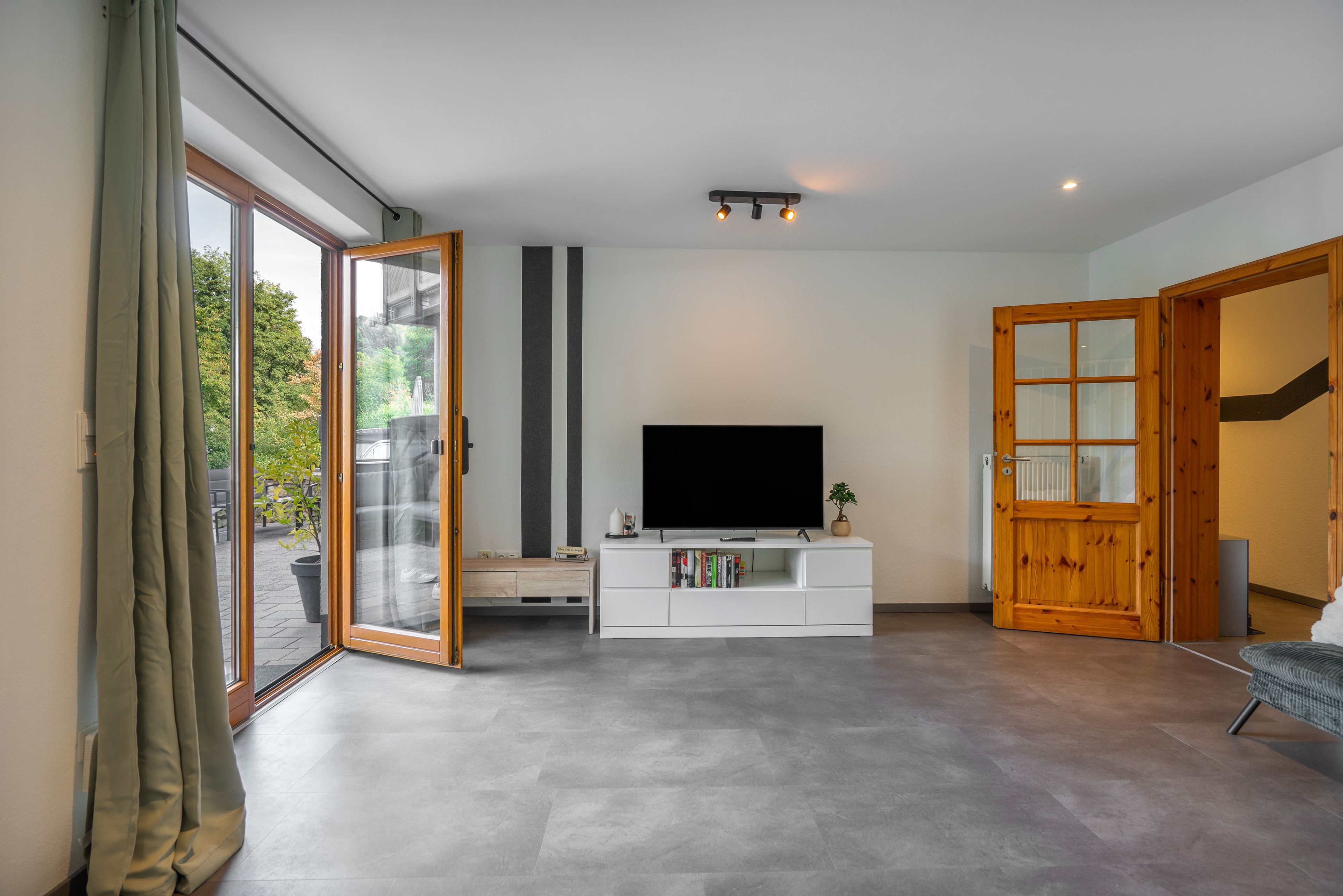 Ein modernes Wohnzimmer mit einem Flachbildfernseher, einer weißen Unterhaltungsanlage und einer Glastür, die zu einem Außenbereich führt.