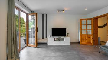 Ein modernes Wohnzimmer mit einem Flachbildfernseher, einer weißen Unterhaltungsanlage und einer Glastür, die zu einem Außenbereich führt.