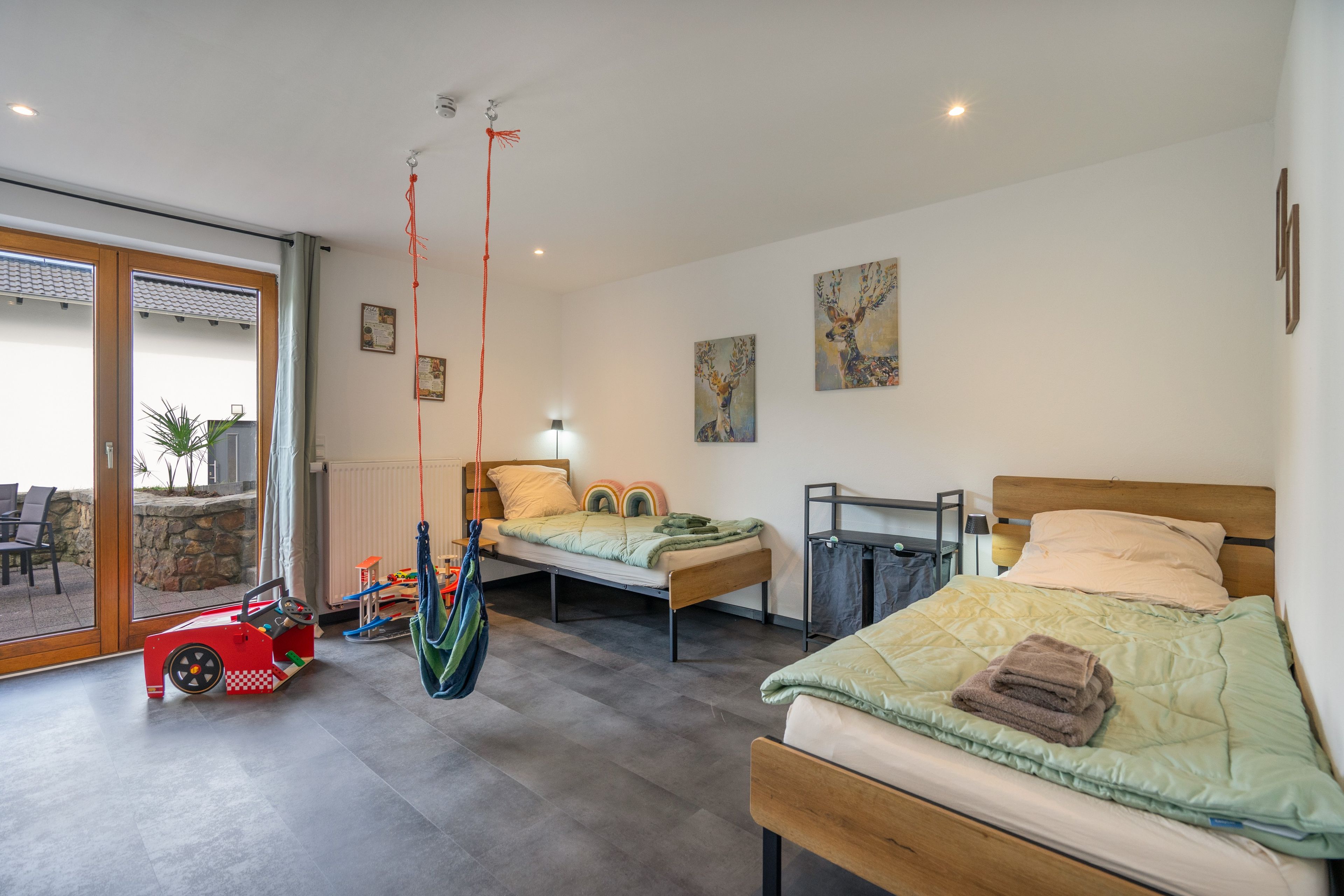 Ein modernes Schlafzimmer mit zwei Betten, einem Hängesessel und einem roten Spielzeugauto.