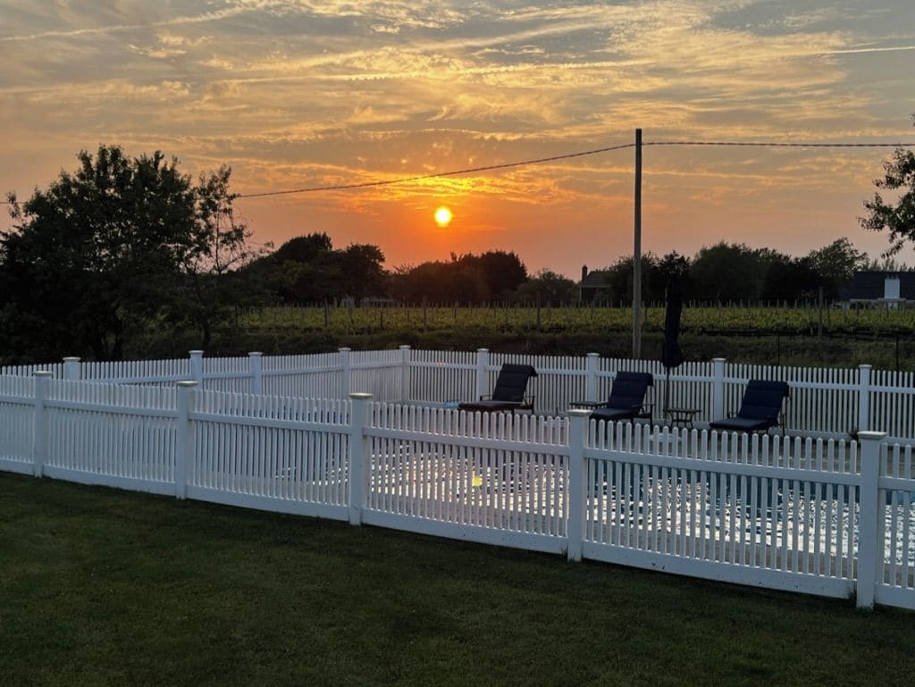 A fenced outdoor area with a sunset in the background, a grassy field, and a few lounge chairs.