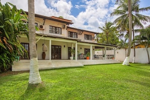 Uma casa de dois andares com varanda coberta, gramado bem cuidado e palmeiras.