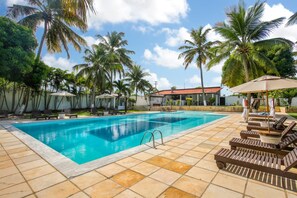 Piscina com espreguiçadeiras e guarda-sóis, rodeada por palmeiras.
