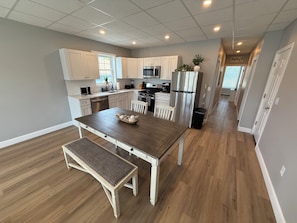 A modern kitchen with white cabinets, stainless steel appliances, and a wooden dining table with a bench.
