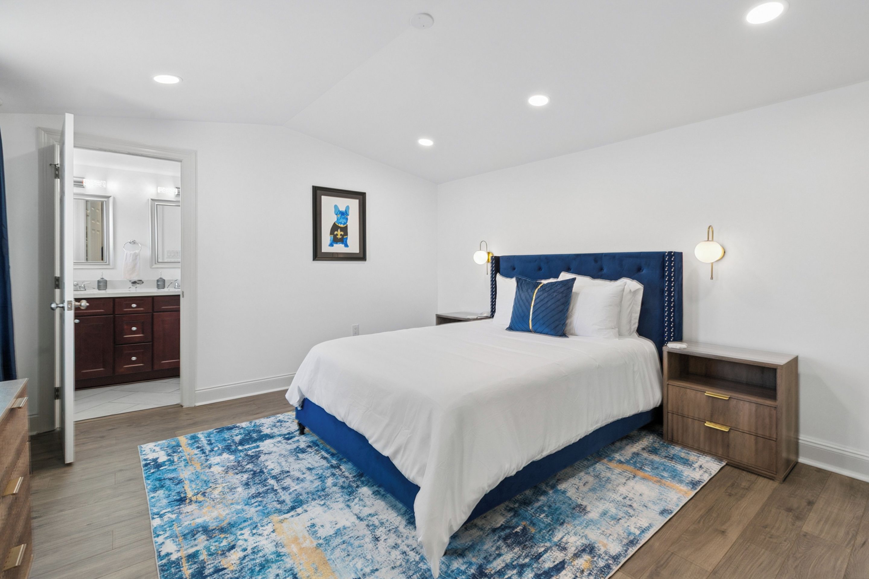 A bedroom with a bed, nightstands, a bathroom with a mirror, and a framed picture on the wall.