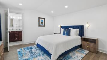 A bedroom with a bed, nightstands, a bathroom with a mirror, and a framed picture on the wall.