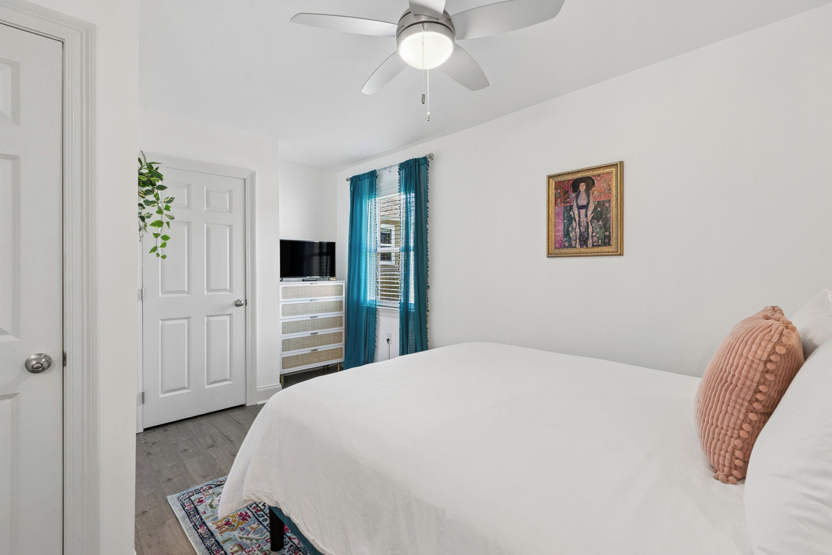 A bedroom with a bed, a ceiling fan, a door, and a window with curtains.