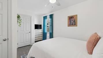 A bedroom with a bed, a ceiling fan, a door, and a window with curtains.