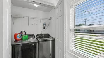 A laundry area with a washing machine and dryer, a drying rack, and a window with blinds.