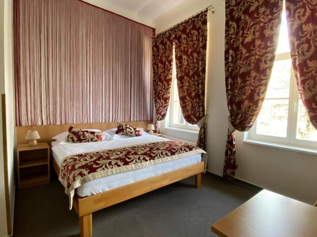 A bedroom with a wooden bed, a nightstand, a lamp, and a window with curtains.