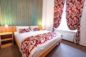 Quarto com cama, mesa de cabeceira, janela com cortinas e parede com linhas verticais.