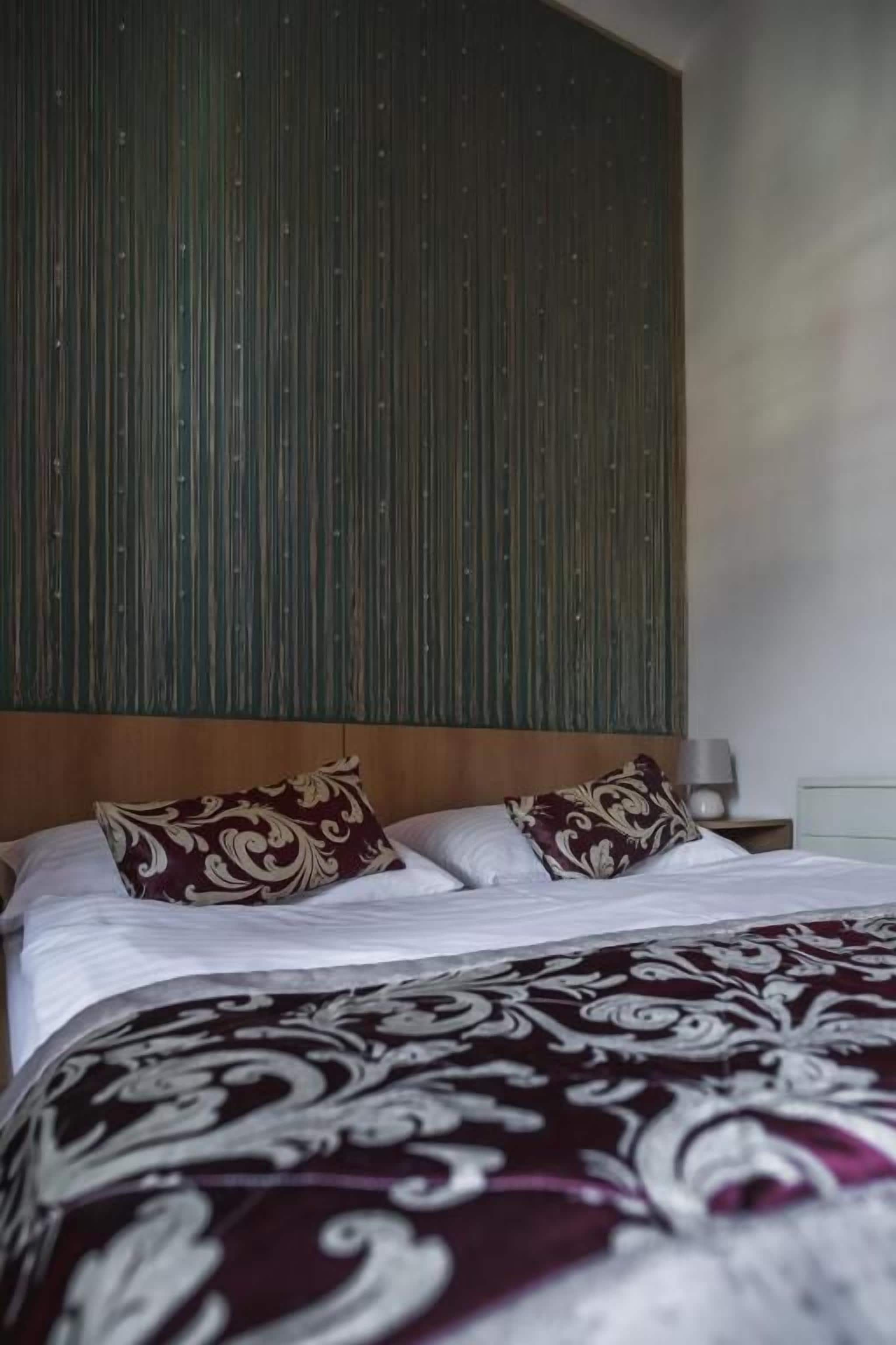 Ein Hotelzimmer mit Bett, Kissen, Kopfteil, Nachttisch und Lampe.