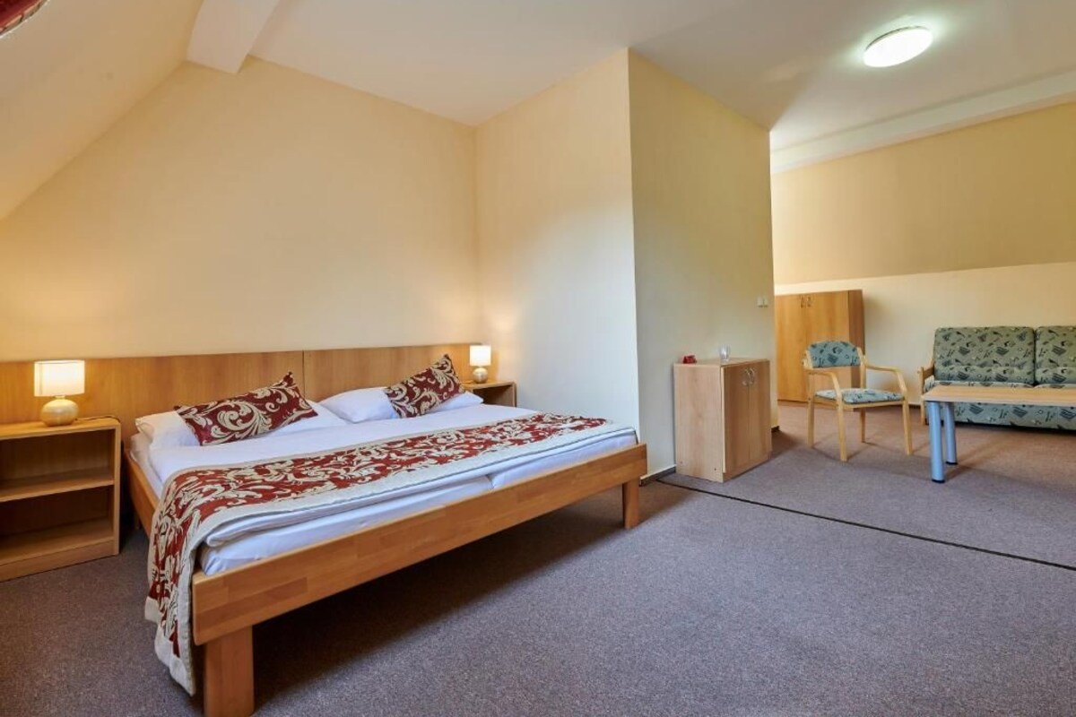 Quarto com cama de madeira, mesas de cabeceira, um guarda-roupa, um sofá e uma pequena mesa.