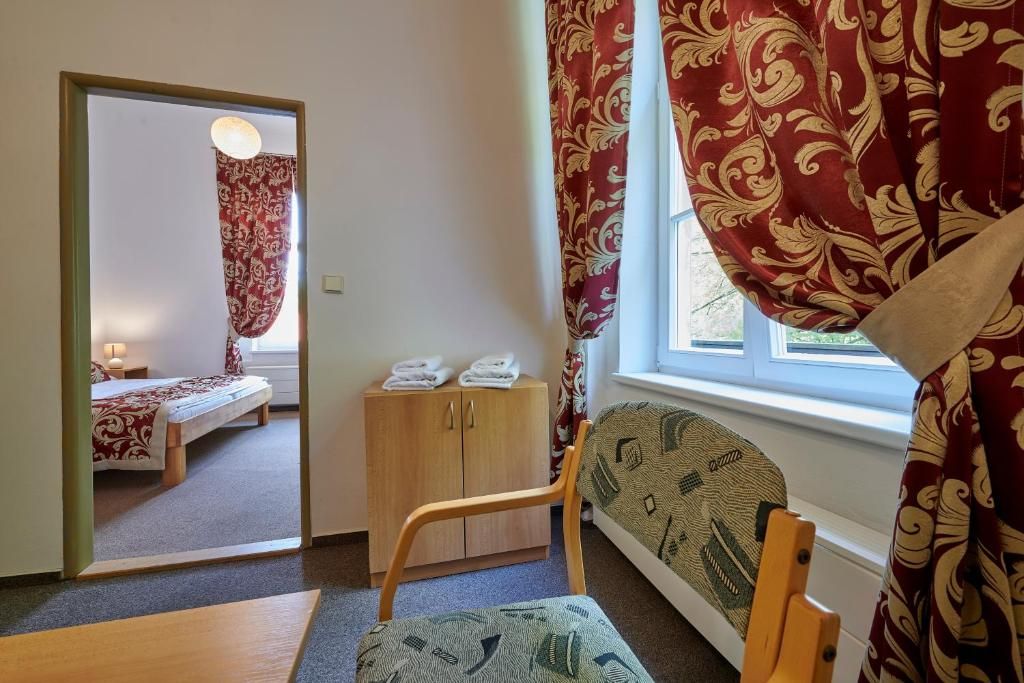 Quarto com cama, um armário de madeira, uma cadeira e janela com cortinas.