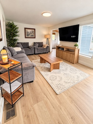 Ein modernes Wohnzimmer mit grauem Sofa, Couchtisch aus Holz und Flachbildfernseher.