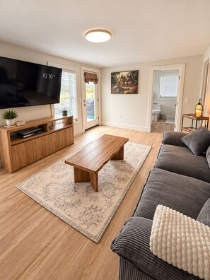 Ein Wohnzimmer mit Flachbildfernseher, einer Holz-Unterhaltungseinrichtung, einem Couchtisch, einer Couch und einem Teppich.