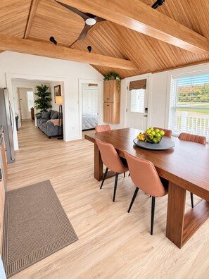 Eine moderne Küche mit Holzbalkendecke, ein Essbereich mit Holztisch und -stühlen sowie ein Blick ins Freie durch große Fenster.