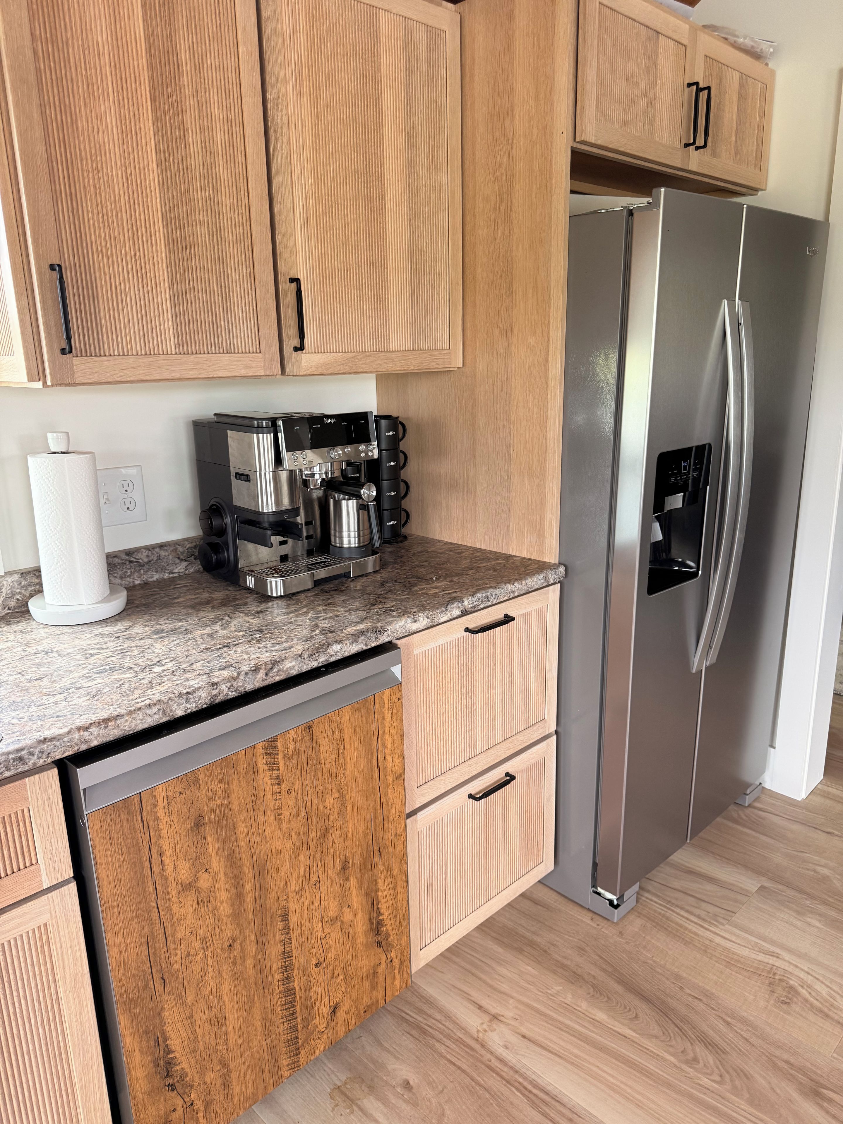 Eine Küche mit Holzschränken, einem Edelstahlkühlschrank, einer Kaffeemaschine und einem Geschirrspüler.
