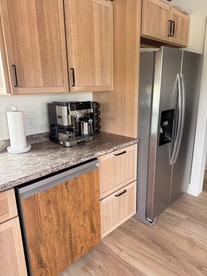 Eine Küche mit Holzschränken, einem Edelstahlkühlschrank, einer Kaffeemaschine und einem Geschirrspüler.