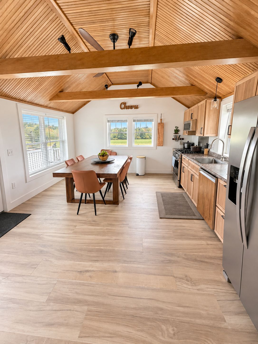 A spacious kitchen with wooden beams, a dining area with a table and chairs, and a view through large windows.