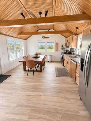 A spacious kitchen with wooden beams, a dining area with a table and chairs, and a view through large windows. - Meadow Place Modern 3BR Belfast Getaway with Deck (Belfast)
