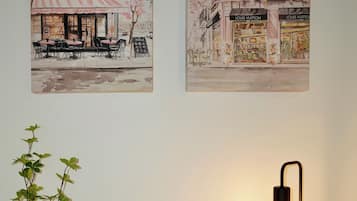 A desk with a potted plant, a lamp, and two wall art pieces depicting urban scenes.