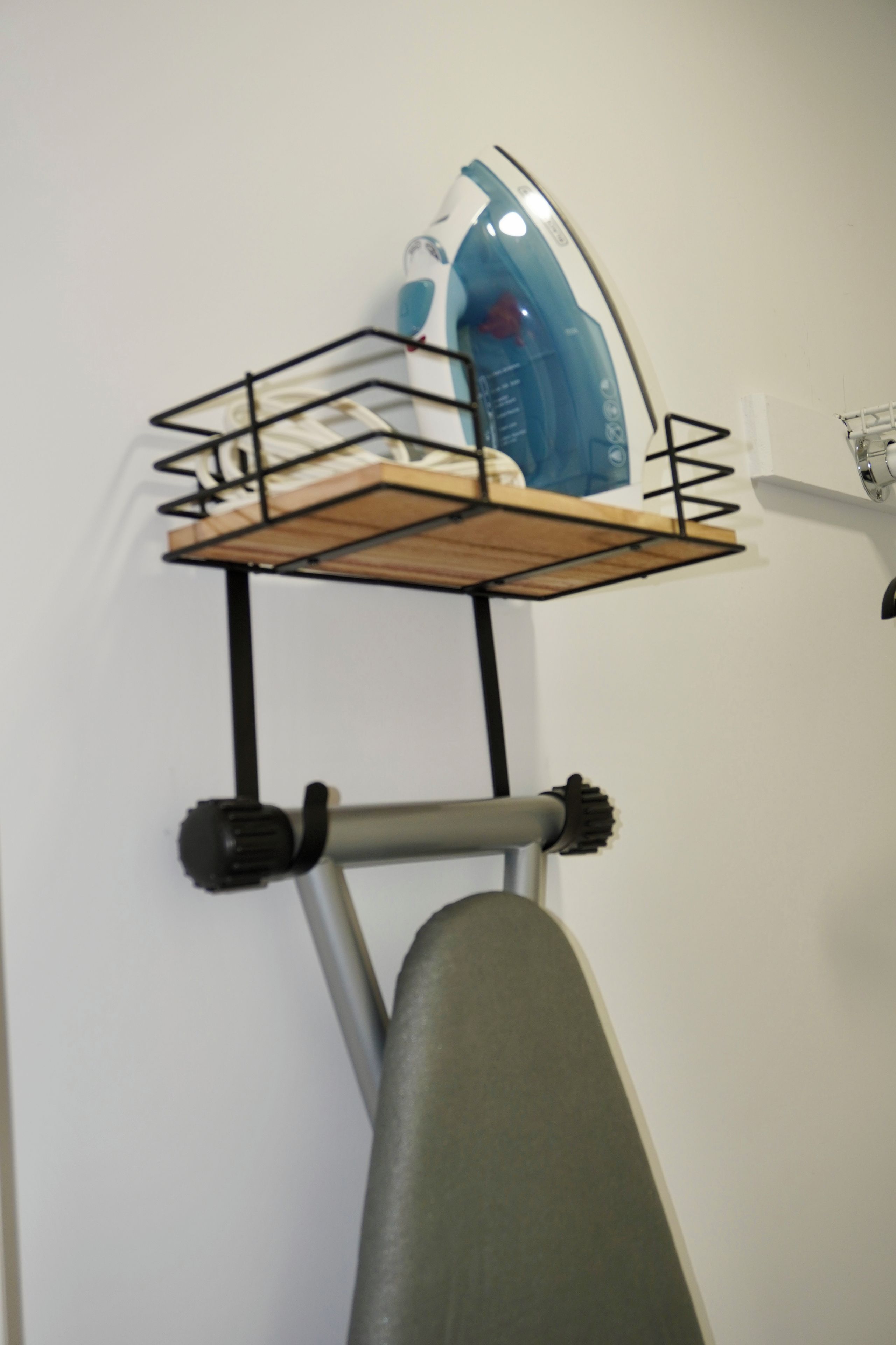 A wall-mounted ironing board with an iron and a basket.