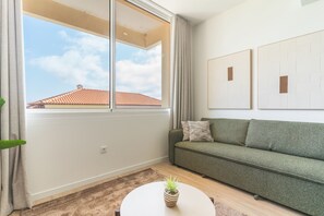 A modern living room with a sofa, a small table with a plant, and a large window with curtains. - Cica Studio by Atlantic Holiday (Santa Cruz)