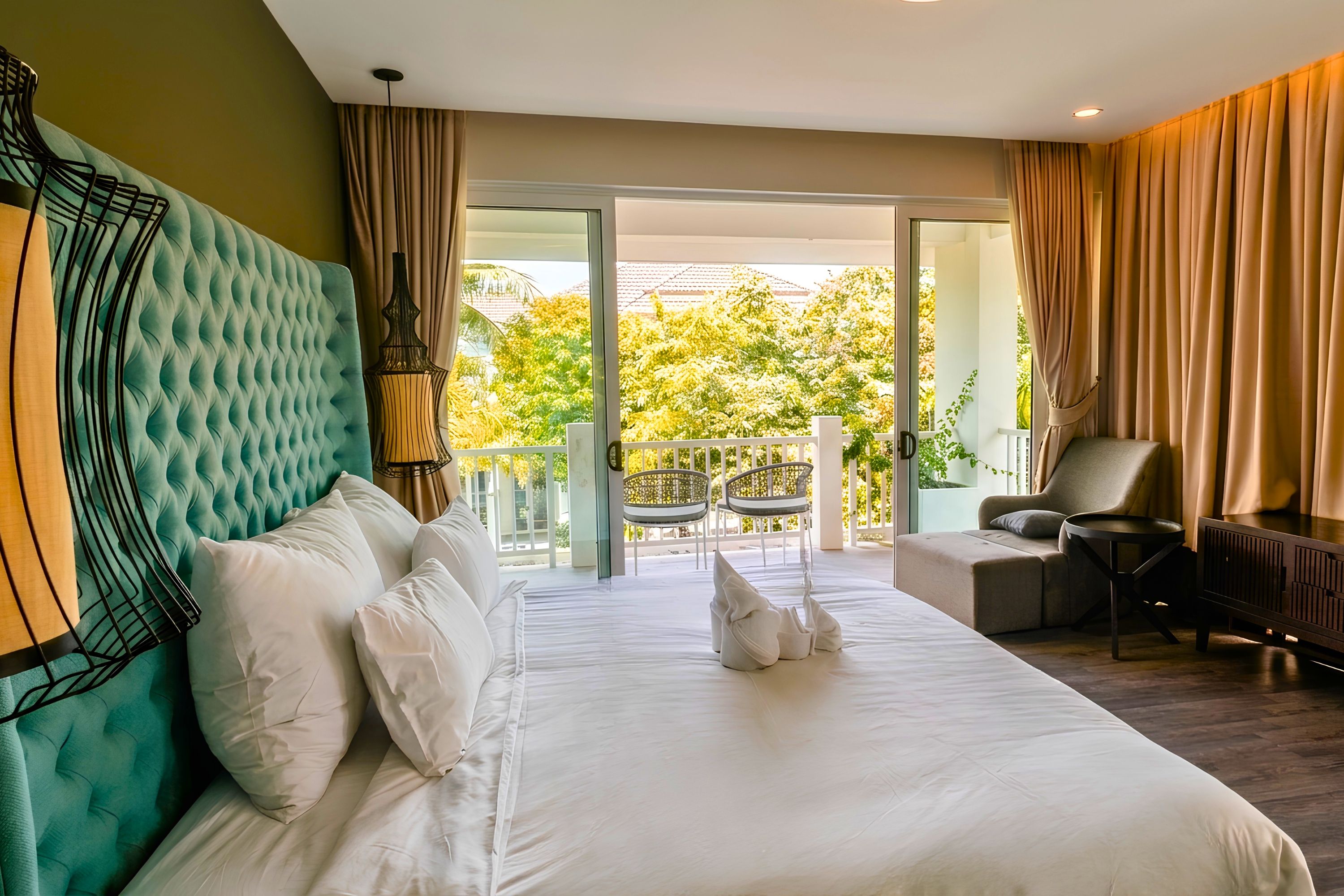 A hotel room with a large bed, a view of the outdoors, a sitting area with a chair and table, and a balcony with a railing.