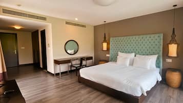 Quarto de hotel com uma cama grande, uma escrivaninha, uma cadeira e um espelho redondo.