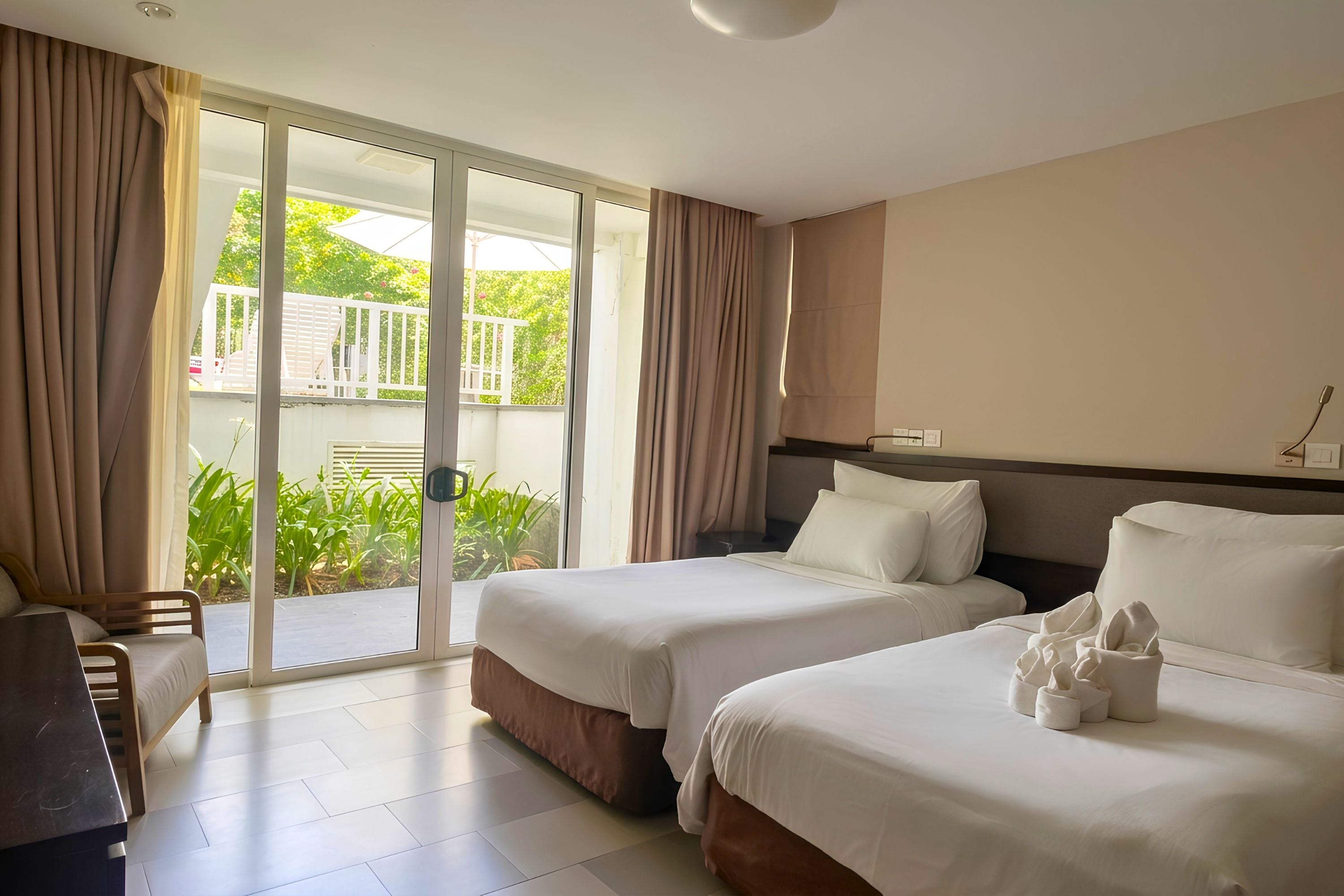 A hotel room with two beds, a desk, and a sliding glass door leading to an outdoor area.