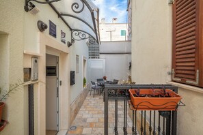 Un estrecho callejón con un pequeño patio amueblado con mobiliario exterior y plantas en macetas.