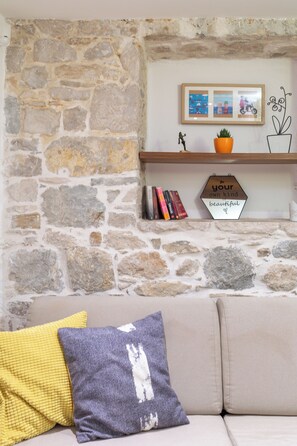 Una pared de piedra con un estante que sostiene libros, un cuadro enmarco y un letrero.